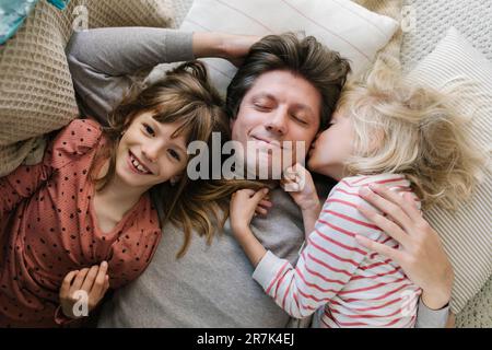 Père heureux allongé avec des filles sur des oreillers à la maison Banque D'Images