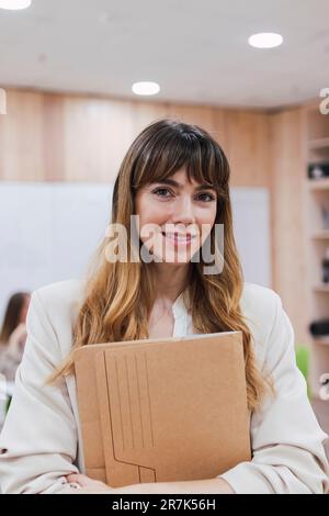Portrait d'une femme d'affaires souriante tenant un dossier au bureau Banque D'Images