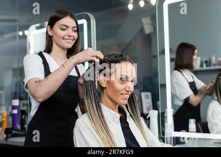 coiffeur et cliente féminine, salon de beauté, coiffeur tatoué faisant des cheveux de femme gaie avec des braïdes, deux queues de cheval, satisfaction de la clientèle, bea Banque D'Images