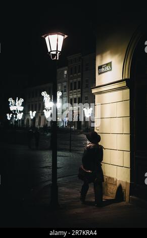 Une femme adulte mature debout à l'extérieur près d'une lampe de rue portant un long manteau dans la rue Stolarska Banque D'Images
