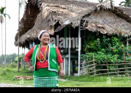 Femme souriante de la tribu galo dans ses vêtements traditionnels posant devant sa maison traditionnelle faite de bambous et de palmiers, assam, inde Banque D'Images