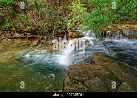 Vue latérale d'une petite chute d'eau en cascade longue exposition qui se répand dans la crique lors d'une journée ensoleillée au début du printemps Banque D'Images