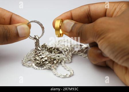 Des chaînes d'argent et un anneau d'argent avec un anneau d'or tenu dans la main sur un fond blanc Banque D'Images