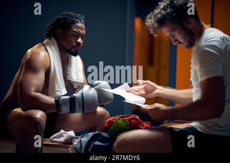 Joueur de boxe déterminé avec le visage sérieux dans les sueurs après l'entraînement se reposant avec son entraîneur, obtenant la consultation. Boxe, sport, concept de style de vie. Banque D'Images