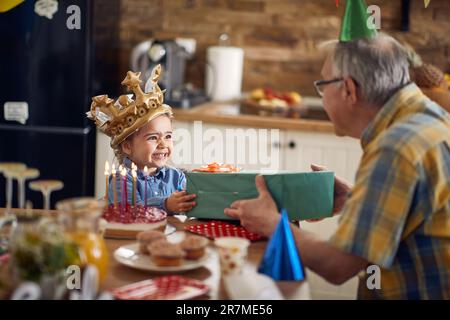 Adorable petite fille portant la couronne dorée se sentant très excitée et reconnaissante d'avoir reçu un cadeau de son grand-père. Belle fête de famille. Banque D'Images