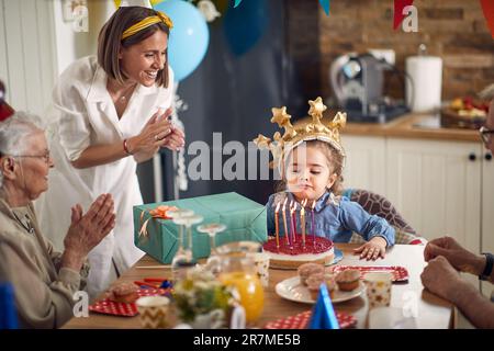 Une petite fille, remplie de joie et d'excitation, souffle les bougies sur son gâteau d'anniversaire, entouré de sa mère aimante, de grand-mère d'émeutes, et de rp Banque D'Images