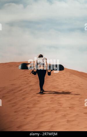 Surf des neiges sur le sable : une femme se carve gracieusement dans une dune, mêlant deux mondes d'aventure en une captivante démonstration de compétence et d'excitation. Banque D'Images