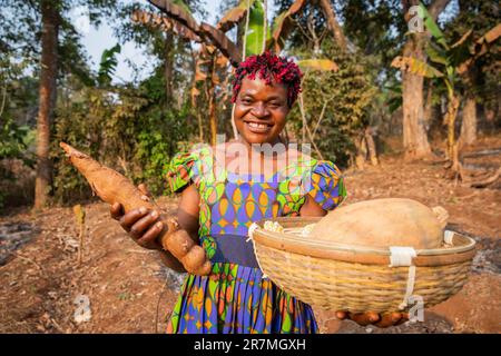 Une paysanne souriante avec son panier de récolte dans les champs, propriétaire d'une petite entreprise en Afrique Banque D'Images