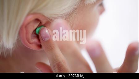 Femme mettant le bouchon d'oreille dans son oreille dans le lit Banque D'Images