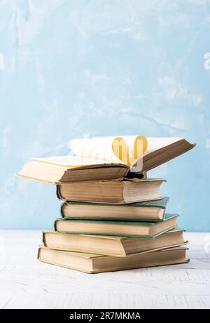 Livre avec des pages ouvertes en forme de coeur et des livres empilés sur le bureau de lecture dans la bibliothèque. Bibliothèque nationale, amateurs de livres jour ou mois. Retour à l'école ou Banque D'Images