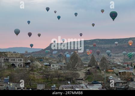 Une photo de ballons à air chaud survolant le parc national historique de Göreme et la ville de Göreme au lever du soleil. Banque D'Images