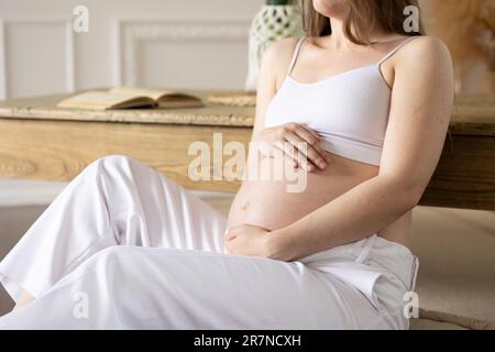 Une fille enceinte s'assoit sur le sol table inclinée gros plan du concept de l'abdomen calme grossesse heureuse future maternité Banque D'Images