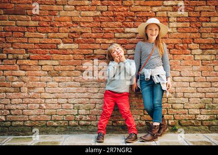 Portrait extérieur de tout petit garçon et fille, enfants élégants posant contre un mur de briques vintage. Mode pour les petits enfants Banque D'Images