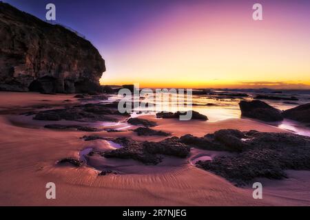 Soleil marin pittoresque sombre sur la plage des grottes de la côte du Pacifique en Australie - marée basse près des rochers. Banque D'Images