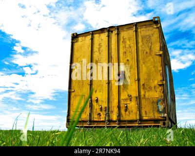 Contenant jaune rouille sur l'herbe verte sous le ciel bleu. Banque D'Images