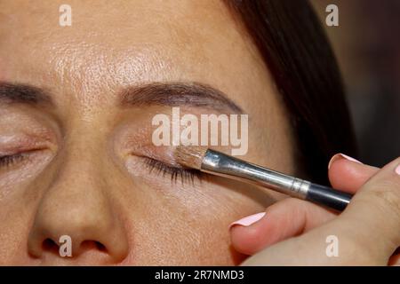 Maquilleuse applique une ombre à paupières . Belle femme visage. Main de visagiste, la peinture de cosmétiques de jeune fille modèle de beauté . Maquillage en cours Banque D'Images