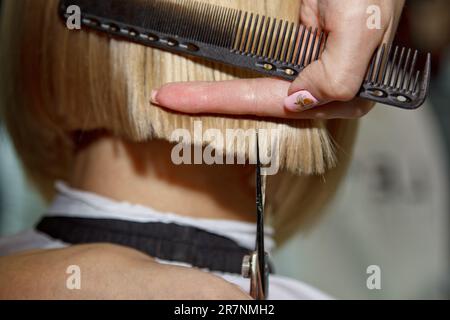 Gros plan d'un coiffeur coupe les cheveux blancs mouillés d'un client dans un salon. Coiffeur coupe une femme. Vue latérale d'un coupe de cheveux à la main avec des ciseaux Banque D'Images