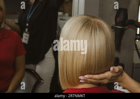 Gros plan d'un coiffeur coupe les cheveux blancs mouillés d'un client dans un salon. Coiffeur coupe une femme. Vue latérale d'un coupe de cheveux à la main avec des ciseaux Banque D'Images