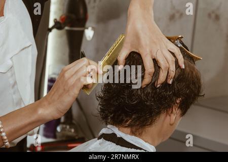 Gros plan d'un coiffeur coupe les cheveux bruns humides d'un client dans un salon. Coiffeur coupe une femme. Vue latérale d'un coupe de cheveux à la main avec des ciseaux Banque D'Images