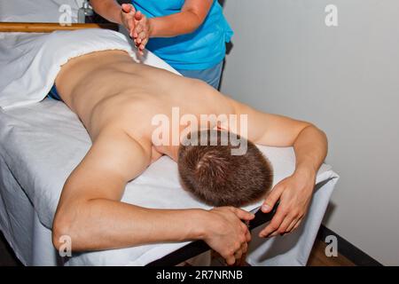 Concept bien-être. Un masseur professionnel donne à un homme un massage thaïlandais avec des bâtons de bambou au spa. Relaxation et récupération après le travail Banque D'Images