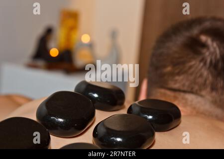 Concept bien-être. Beau jeune homme se relaxant sous l'effet stimulant d'un massage traditionnel aux pierres chaudes dans un spa de luxe et centre de bien-être. Enreg Banque D'Images