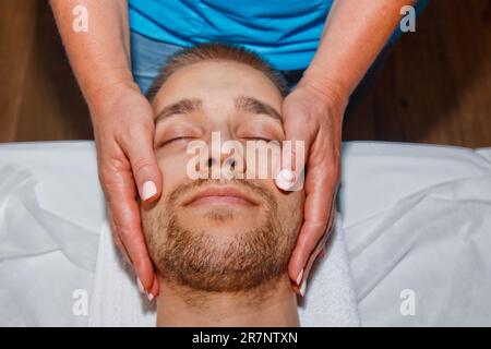 Concept bien-être. Un masseur professionnel offre à un homme un massage du visage thaïlandais avec des bâtons spéciaux dans un centre de spa. Relaxation et récupération après le travail Banque D'Images