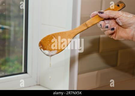 la main féminine pétrit la pâte à base de lait de beurre et de farine dans un bol en métal avec un fouet en bois dans la cuisine. Banque D'Images