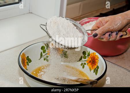 tamisage de la farine à la main de la femme à travers le tamis de farine manuel dans un bol espace de copie en gros plan. cuisson de la pâte. appareil de cuisine en métal. Banque D'Images