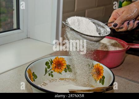 tamisage de la farine à la main de la femme à travers le tamis de farine manuel dans un bol espace de copie en gros plan. cuisson de la pâte. appareil de cuisine en métal. Banque D'Images