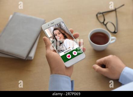 Homme regardant le profil de femme sur le site de rencontres par téléphone portable à la table, gros plan Banque D'Images