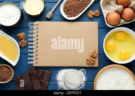 Livre de recettes vierge entouré de différents ingrédients sur une table en bois bleu, plat. Espace pour le texte Banque D'Images