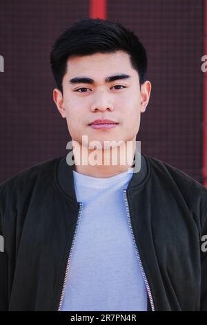 Portrait vertical d'un beau étudiant chinois sérieux habillé de vêtements décontractés, regardant pensive à la caméra avec une expression confiante et jeune sur son visage. Vue de face d'un homme asiatique. Photo de haute qualité Banque D'Images