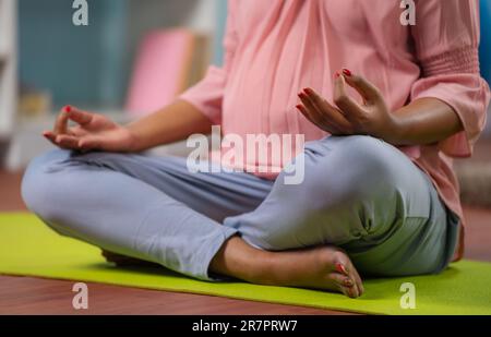 Gros plan de femme enceinte indienne dans lotus pose faire de la méditation sur le tapis de yoga à la maison - concept de pleine conscience, de détente et d'auto-soins pendant Banque D'Images