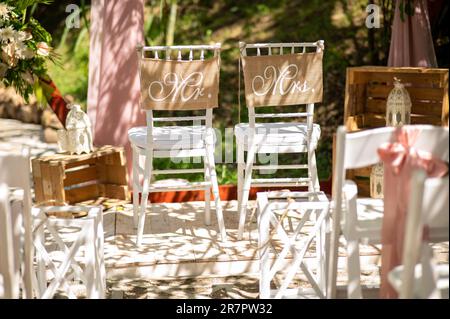 Cette photo de stock présente deux chaises blanches avec ruban et des panneaux avec les mots M. et Mme dessus, parfait pour une cérémonie de mariage Banque D'Images