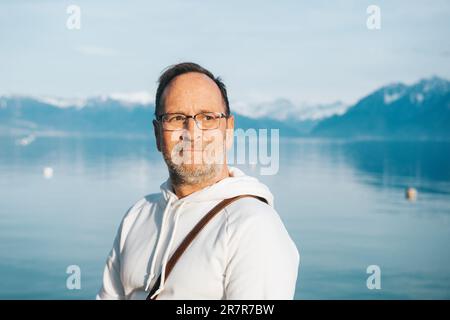 Portrait d'un beau homme admirant un beau lac avec des montagnes, portant un sweat-shirt blanc Banque D'Images