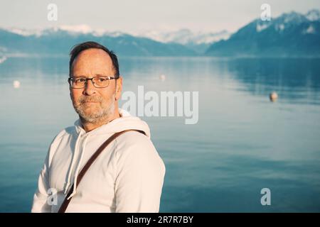 Portrait d'un beau homme admirant un beau lac avec des montagnes, portant un sweat-shirt blanc Banque D'Images