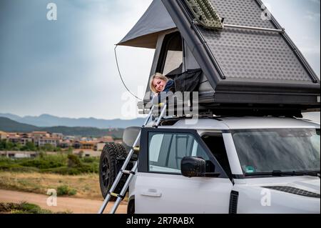 Femme blonde campant dans une tente de toit au sommet d'un véhicule tout-terrain 4x4 blanc Banque D'Images