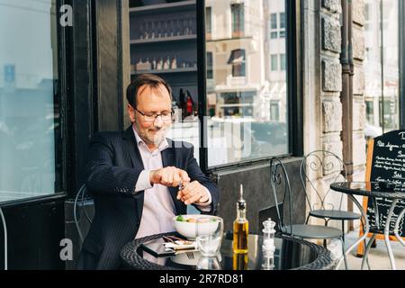 Homme d'affaires qui déjeunait sur une terrasse dans un café en plein air, portant un costume. Salade verte saine avec saumon Banque D'Images