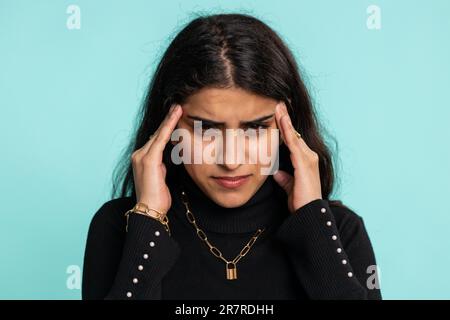 Jolie femme arabe indienne dans les temples de frottement de chandail pour traiter le problème de mal de tête, souffrant de tension, migaine, stress, grimacing dans la douleur, l'hypertension artérielle est isolée seule sur fond de paroi bleue Banque D'Images