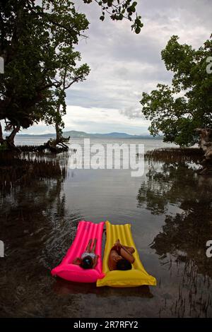 Deux enfants, un frère et une sœur, se détendent sur leurs radeaux gonflables dans les eaux peu profondes de la mangrove. Bunaken, Sulawesi du Nord, Indonésie. Banque D'Images