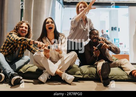 Groupe de collègues multiraciaux et multiethniques s'amusant et riant en jouant à des jeux électroniques au bureau. Ils font une pause au travail Banque D'Images