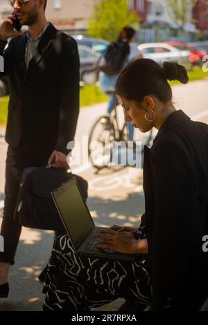 Une femme d'affaires magnifique travaille à l'extérieur, assise sur un banc tandis qu'un homme d'affaires charmant passe devant elle Banque D'Images