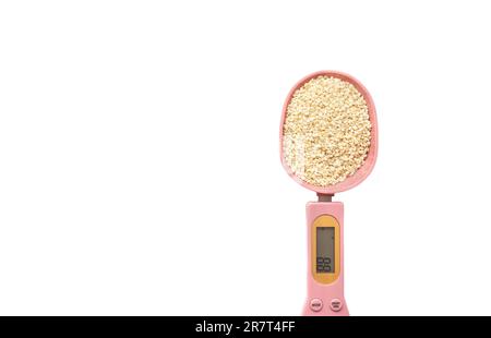 Graines de sésame blanc dans une cuillère de mesure électronique rose sur fond blanc. Superaliments, concept de saine alimentation et régime de céto Banque D'Images