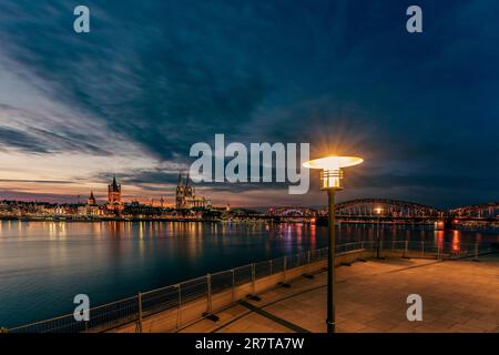 Vue sur la cathédrale de Cologne avec le pont Hohenzollern à la tombée de la nuit et un lampadaire en premier plan, en Allemagne Banque D'Images