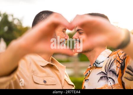 Portrait d'un petit ami gay et d'une petite amie faisant un geste de coeur ou d'amour au coucher du soleil dans un parc de la ville. Diversité et concept lgbt Banque D'Images