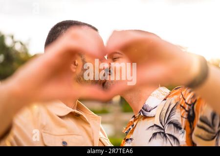 Portrait d'un petit ami gay et d'une petite amie faisant le coeur ou l'amour gestuelle embrassant au coucher du soleil dans un parc de la ville. Diversité et concept lgbt Banque D'Images