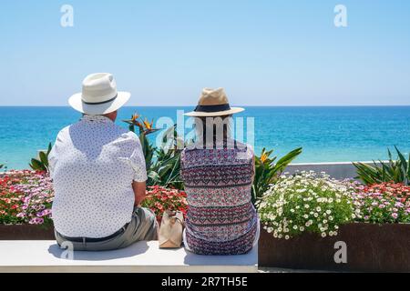 Homme et femme assis sur un banc public et donnant sur le petit jardin et la plage à la mer et à l'horizon, Quinta do Lobo, Algarve, Portugal Banque D'Images