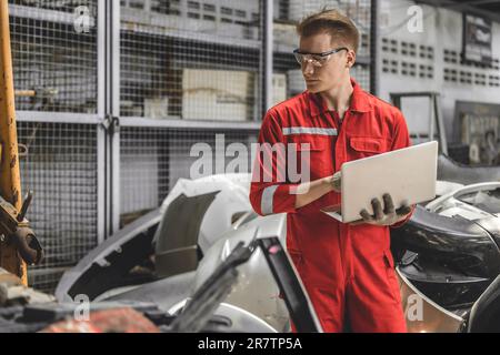 Ancien employé de l'entrepôt de pièces de voiture d'occasion qui vérifie les stocks dans le garage. Employé travaillant dans la gestion des pièces automobiles de chantier de recyclage. Banque D'Images