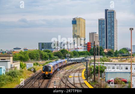 Un train de voyageurs électriques de banlieue South Western Railway sur des voies à l'extérieur de la gare de Woking avec des gratte-ciels de Victoria place sur la ligne d'horizon Banque D'Images
