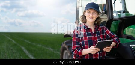 Femme agriculteur avec une tablette numérique à côté d'un tracteur agricole Banque D'Images